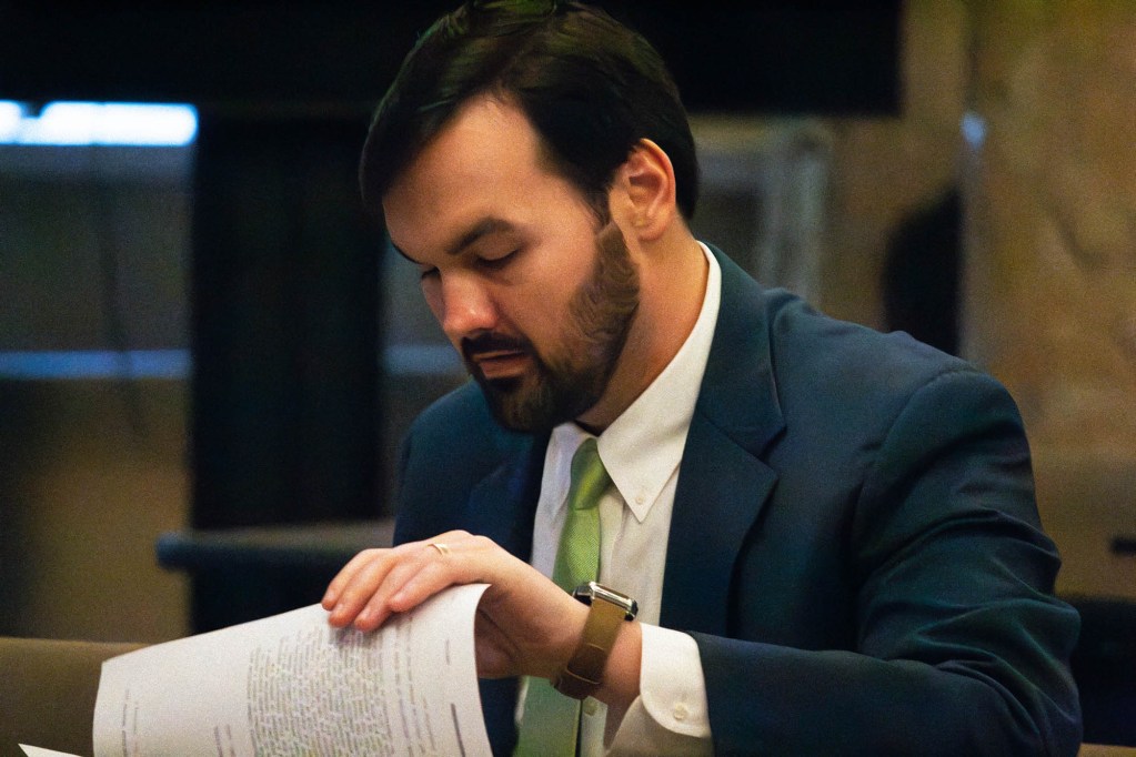 A man in a blue suit flips through papers on a desk