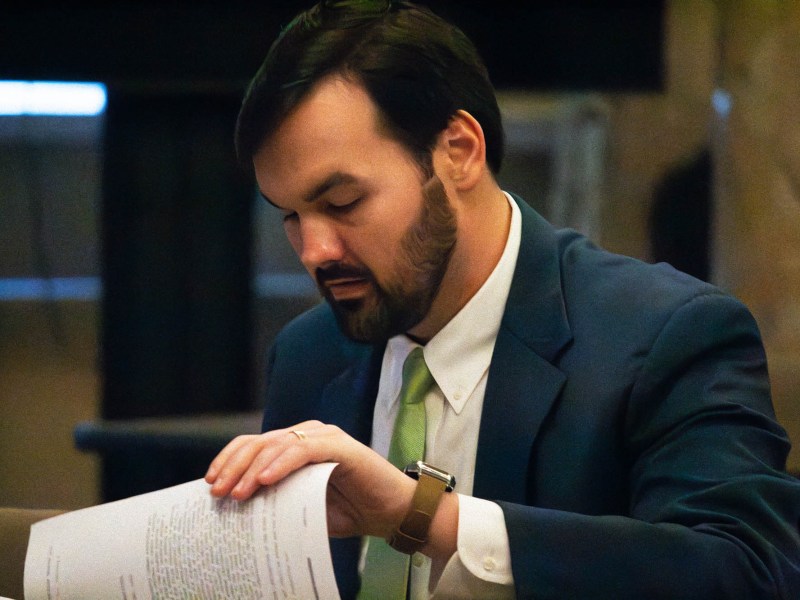 A man in a blue suit flips through papers on a desk
