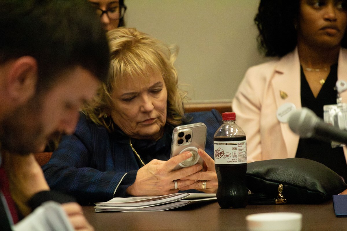 A blonde woman in a meeting room looks at her cell phone