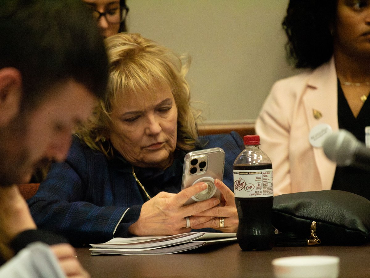 A blonde woman in a meeting room looks at her cell phone