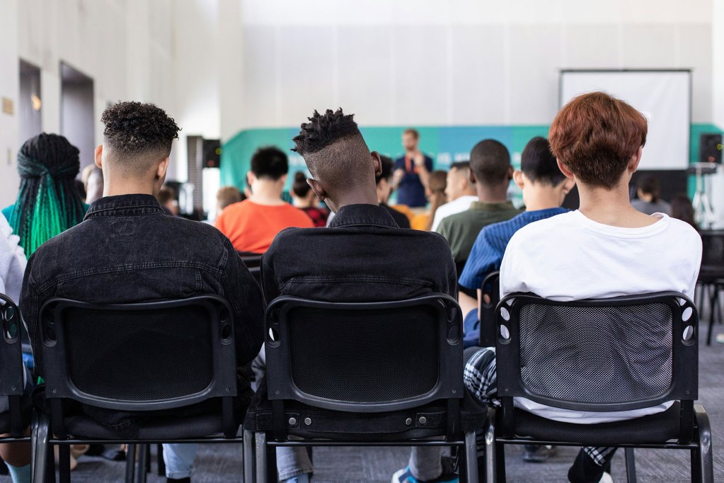 3 young men sitting in a chair in the back of a room