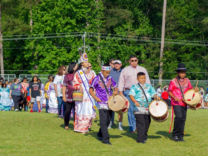 Boys with drums lead a long line of people in colorful dress