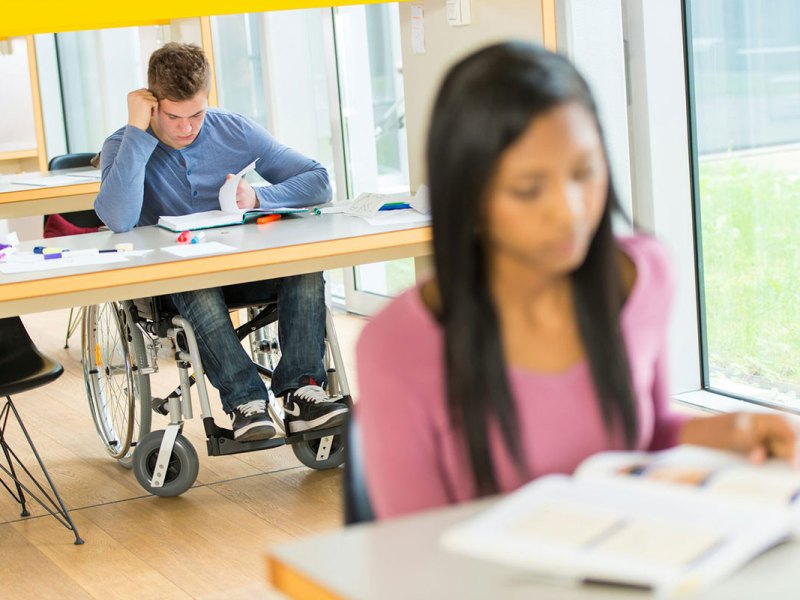 Students sit in a classroom reading, one is in a wheelchair