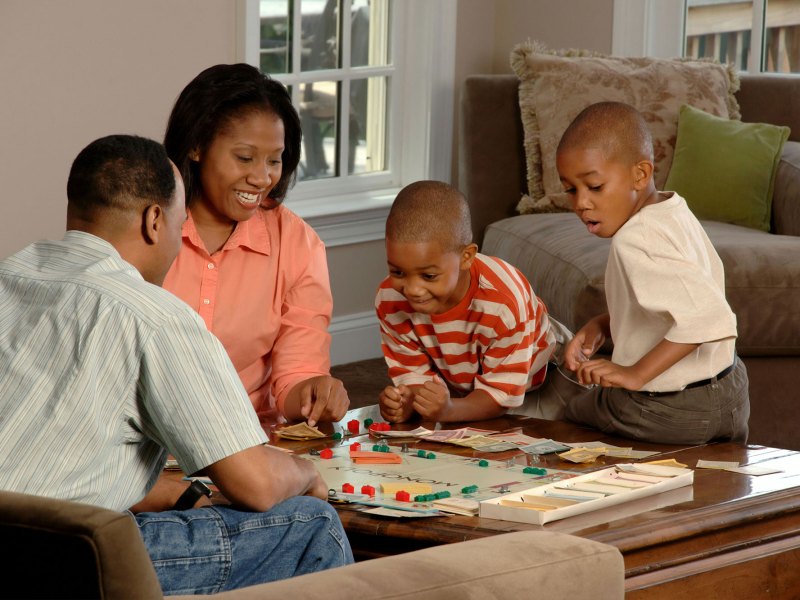 Parents and two children sit around and play monopoly together