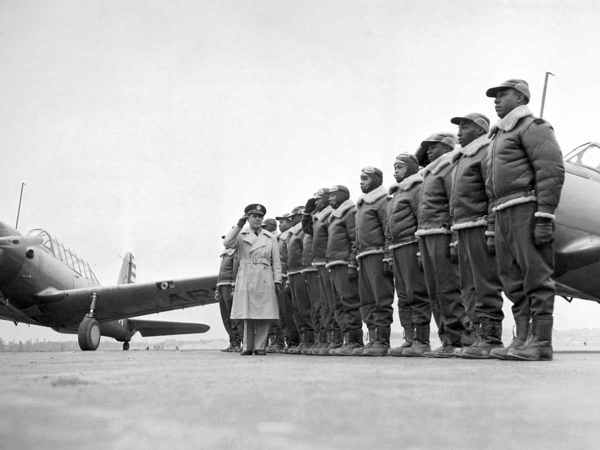 A major reviews a line of black airman standing before some army planes