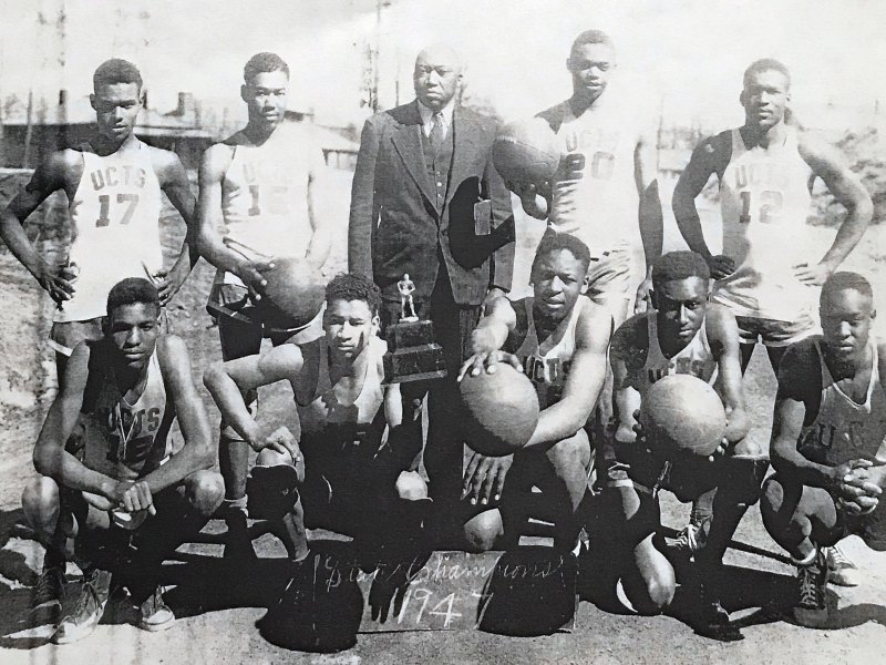 A black and white photo showing a row of standing people behind a row of kneeling people in basketball clothes