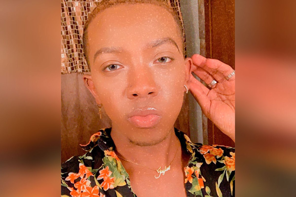 A person in a dark floral top with a gold necklace that reads Jay Lee in script