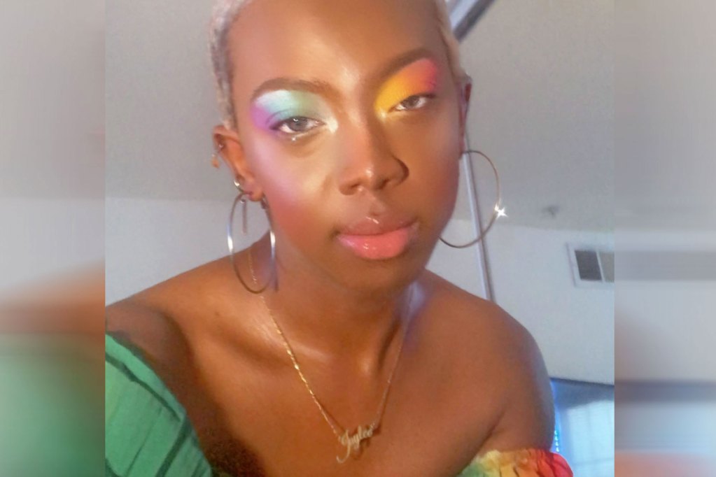 A person with a necklace that says Jay Lee in script, wearing a rainbow and green top and rainbow eyeshadow