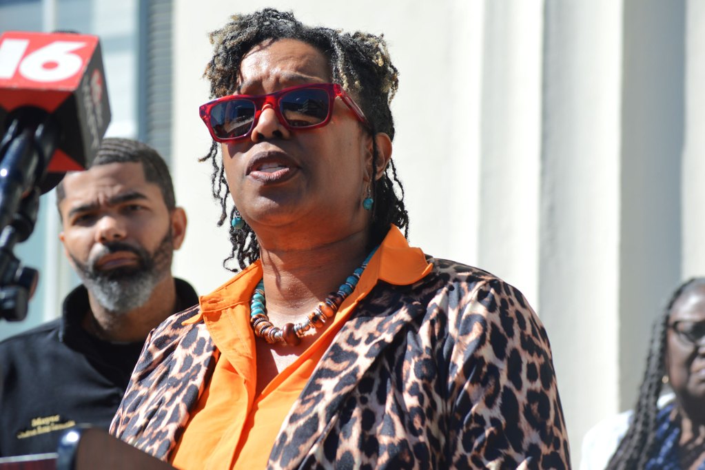 A woman in a leopard print top speaks at a press conference