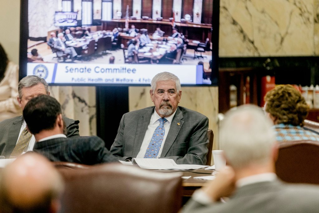 People sitting around a table, the screen behind them reads Senate Committee