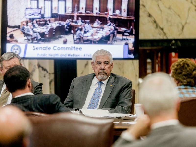 People sitting around a table, the screen behind them reads Senate Committee