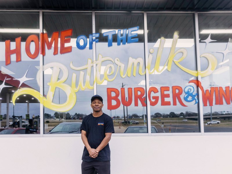 Man in front of a building that reads Home of the Buttermilk Buger & Wings