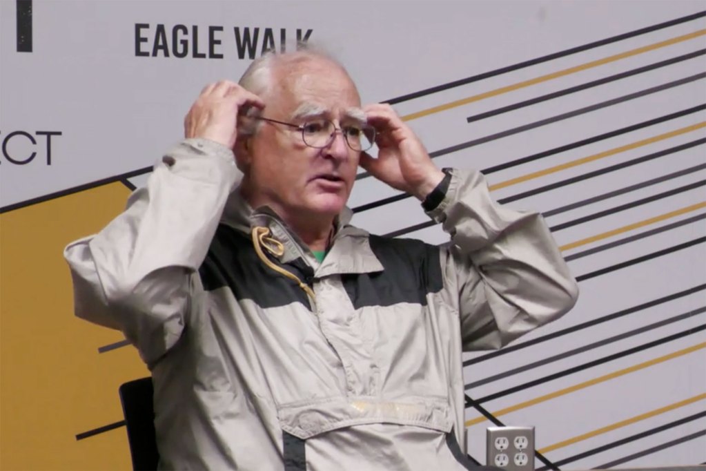 A man speaks on a stage with the words "Eagle Walk" visible behind him