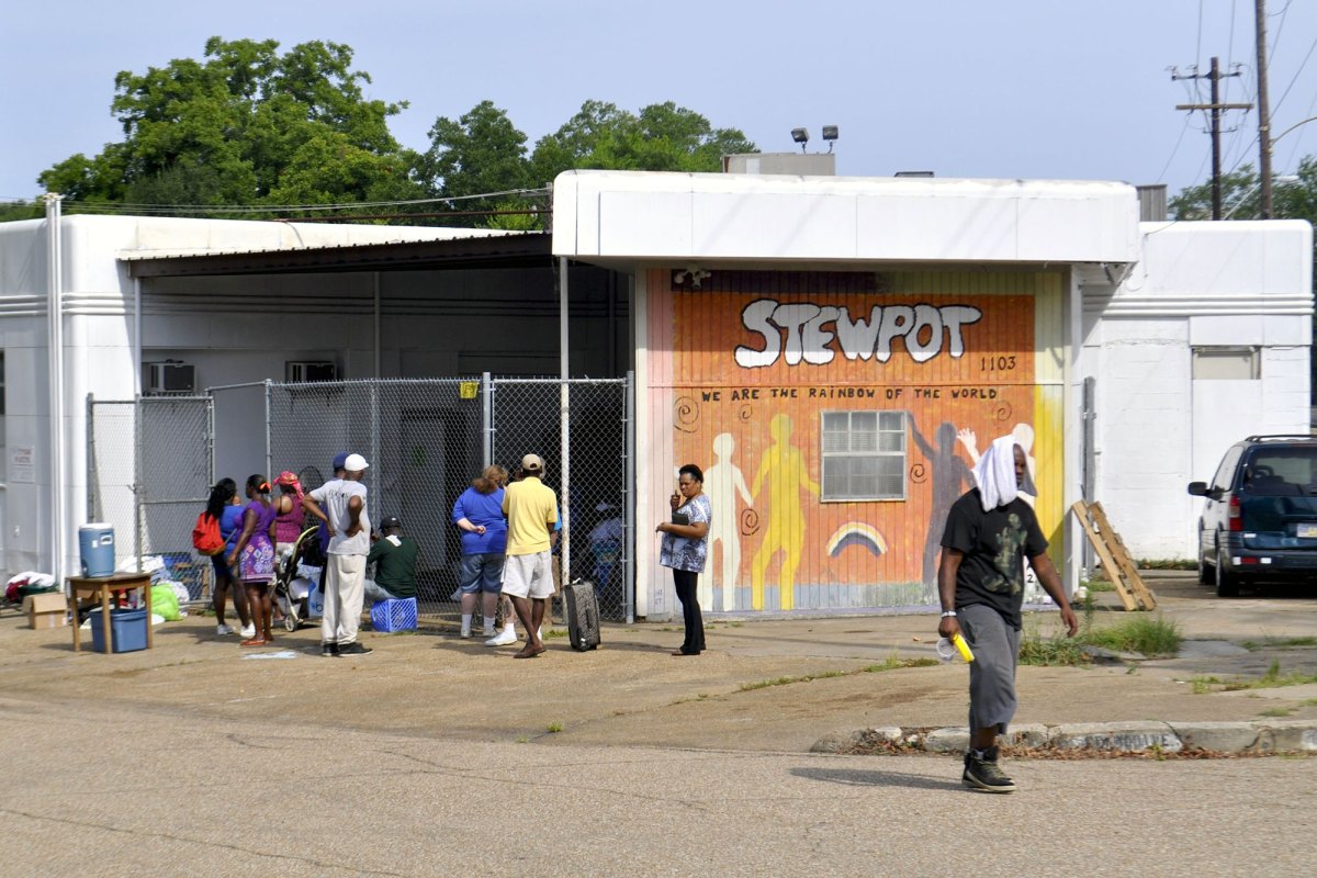 People walk around a building with a hand painted sign reading STEWPOT We are the Rainbow of the World