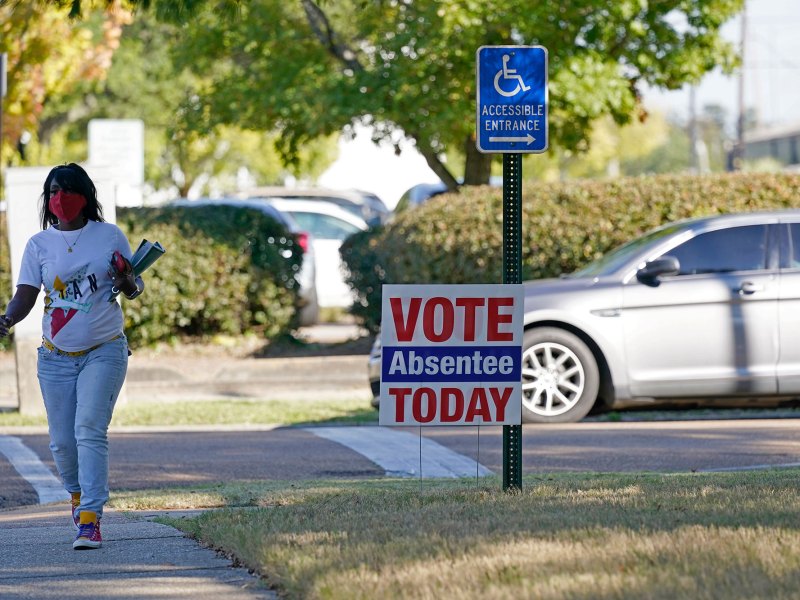 A woman walks past a sign that reads Vote Absentee Today