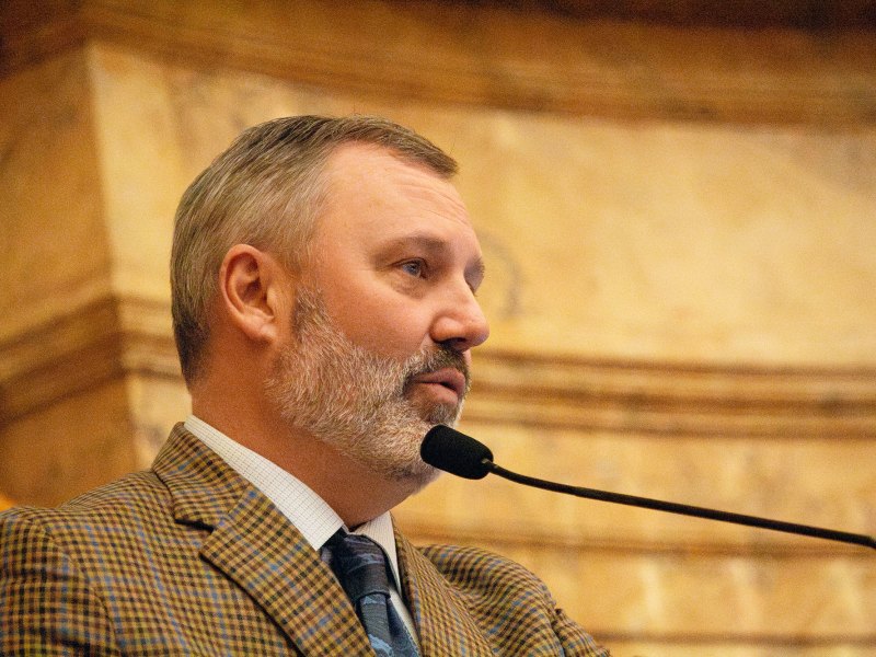 Speaker of the House Jason White speaks into black mic wearing a plaid suit jacket.