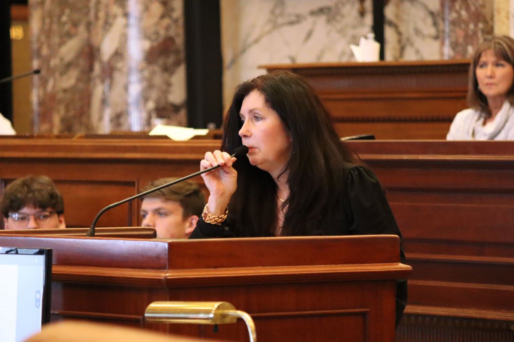 A woman speaks into a microphone while standing at a podium.