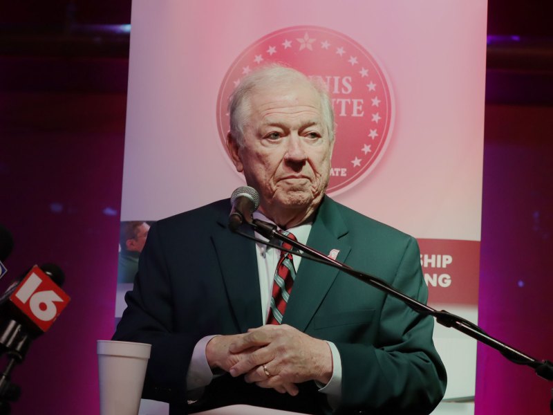 Haley Barbour, an old man with white hair, stands at a microphone