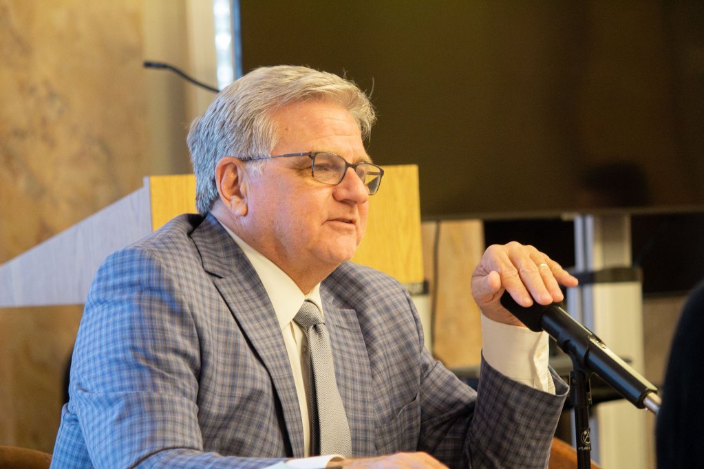 Man with plaid jacket and glasses holds his hand over a mic