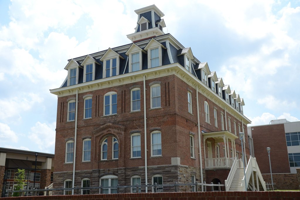 Tall brown brick building with blue clouds behind it.