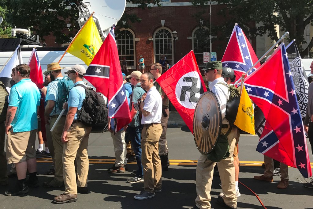Men in white and blue shirts walking with confederate flags in a parade.
