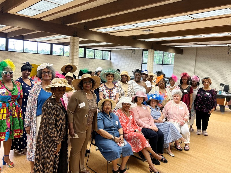 Women in hats stand together in a room for a photograph.