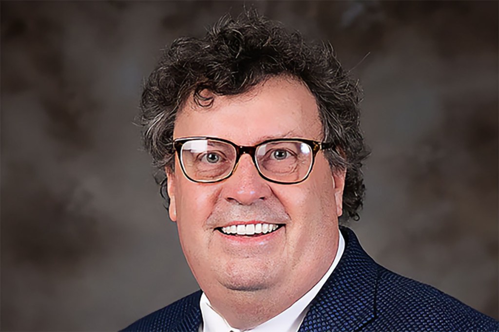 a headshot of a man in glasses smiling