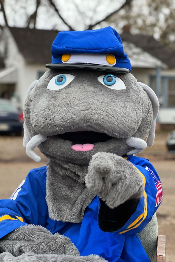A grey and blue catfish festival mascot points at the photo