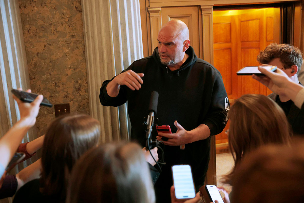 A man in a black hoodie speaks to reporters in legislative building