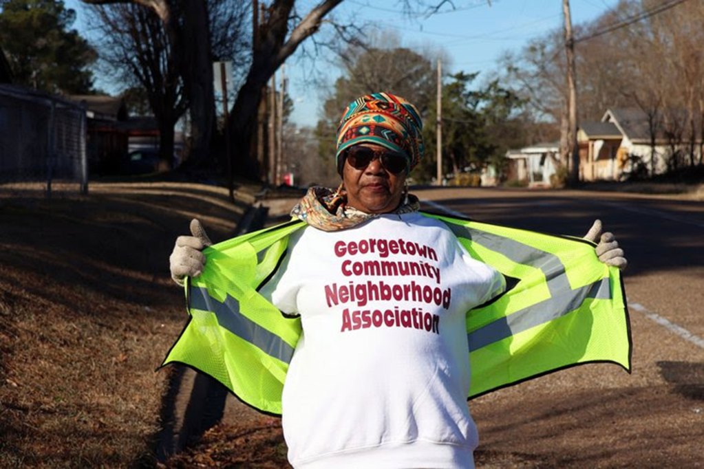 a photo of a woman standing on a residential street wearing a shirt that says, “Georgetown Community Neighborhood Association.”