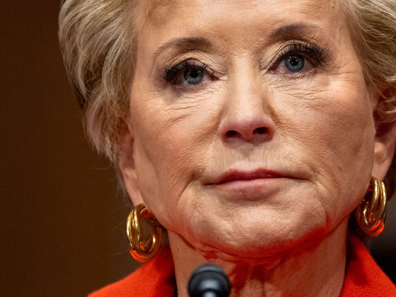 A closeup of Linda McMahon at a mic, wearing a red top and gold earrings