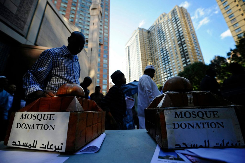 Boxes with 'Mosque Donation' written on them sit on a table as people walk around.