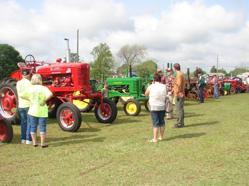 Men and women walking around to view red and green old school tractors.