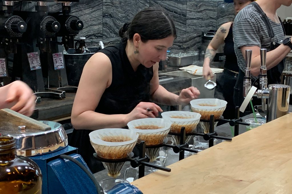 A woman doing a coffee demonstration wearing a black shirt.