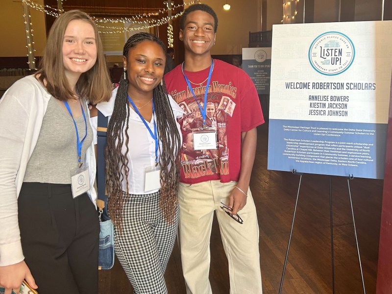 Scholars pose together for a photo right next to a white blue sign that says, "Welcome Robertson Scholars".