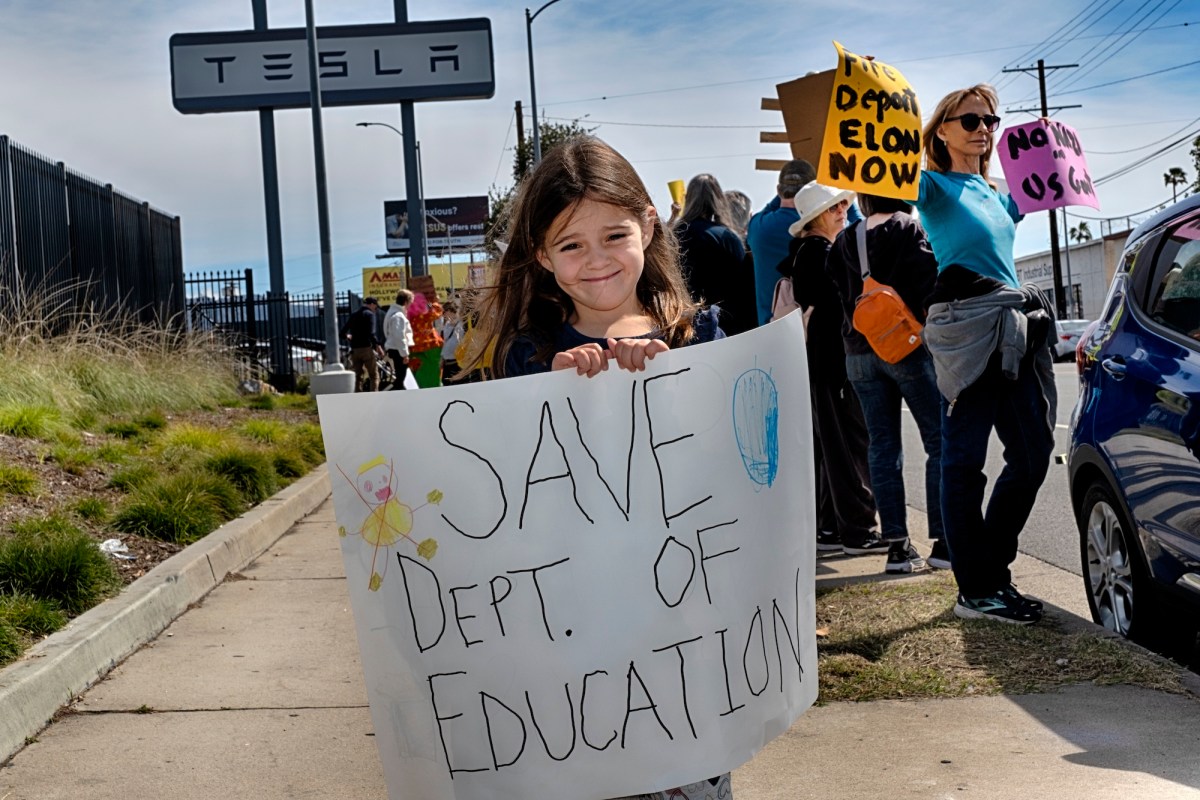 A young girl holds up a sign with a group of protestors behind her
