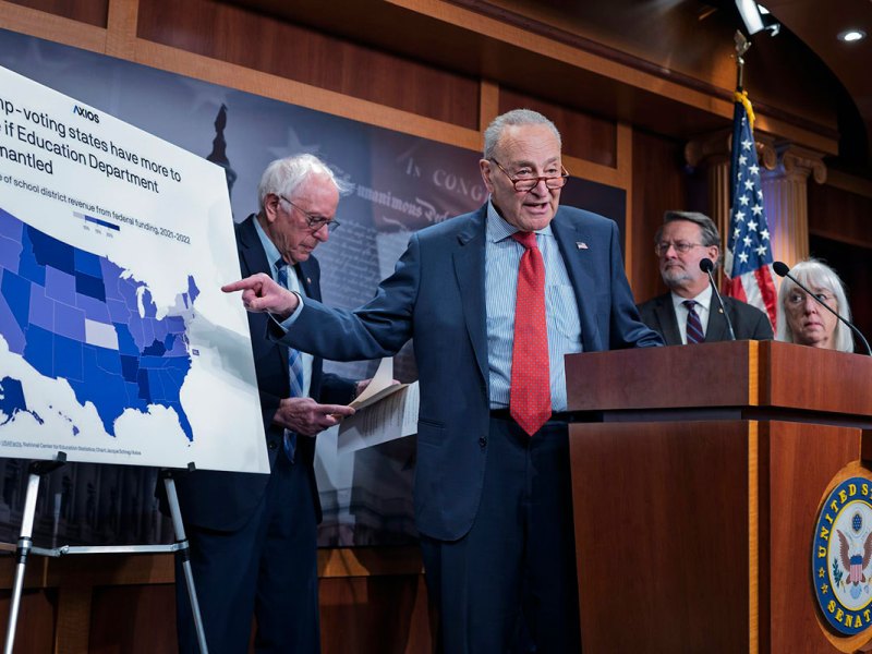 Four people stand on a stage, one pointing at an easel with a map of the US and the title Trump-Voting states have more to lose if Education Department dismantled