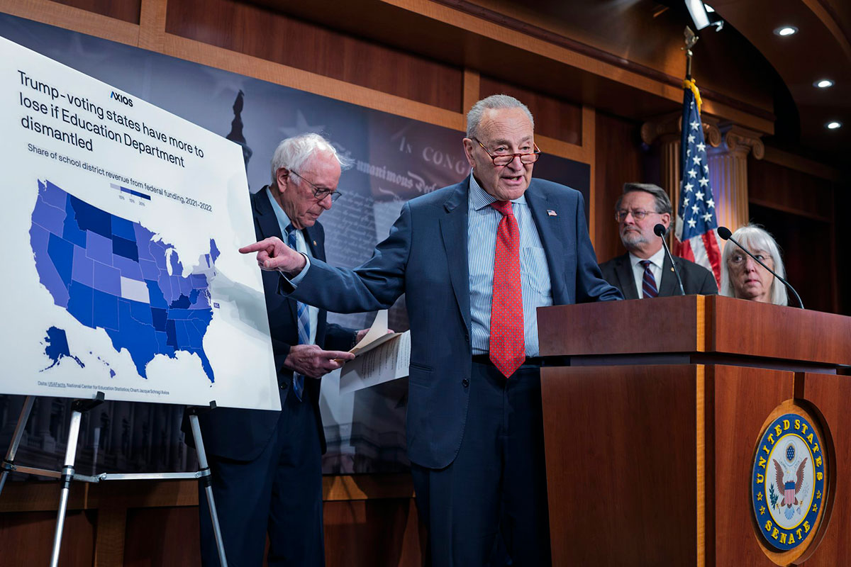 Four people stand on a stage, one pointing at an easel with a map of the US and the title Trump-Voting states have more to lose if Education Department dismantled