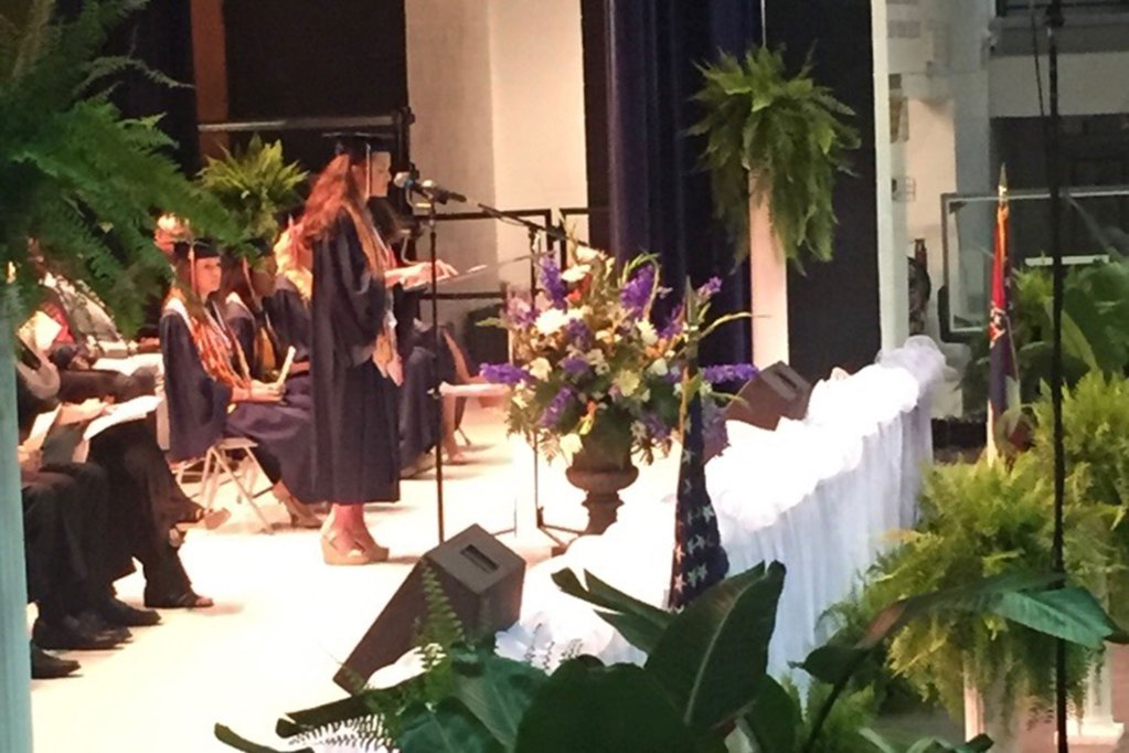 A young woman speaking at a graduation ceremony wearing a black cap and gown