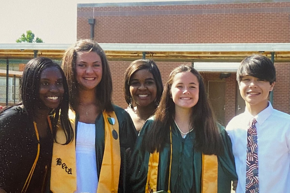 Young women and a man stand together in this photo wearing a green and yellow cap and gown
