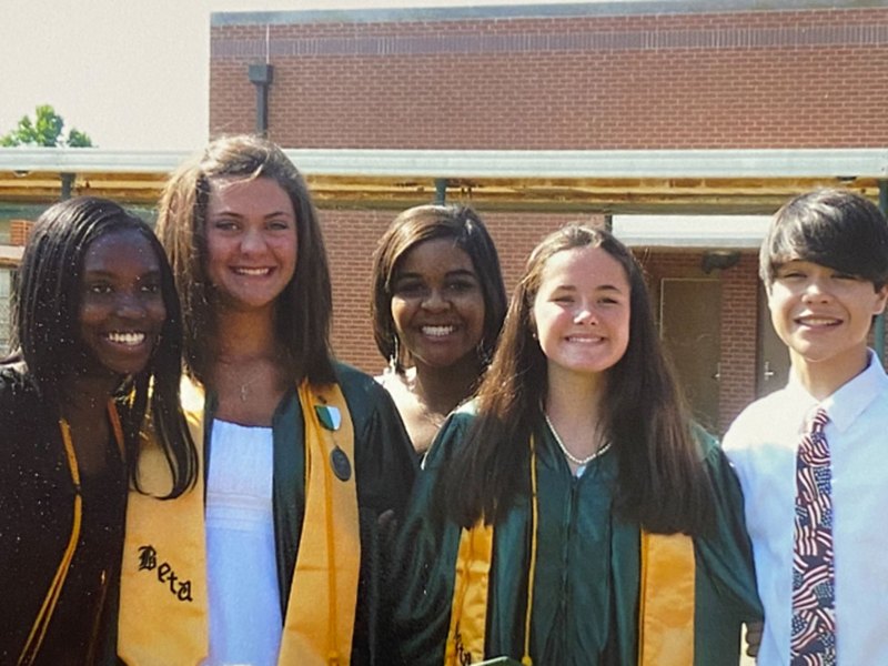 Young women and a man stand together in this photo wearing a green and yellow cap and gown