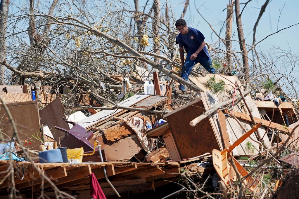 A teen walks over a huge pile of household tornado debris