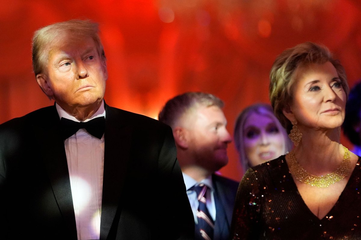 A Man and women wearing formal black clothes stand next to each other in front of an orange background.