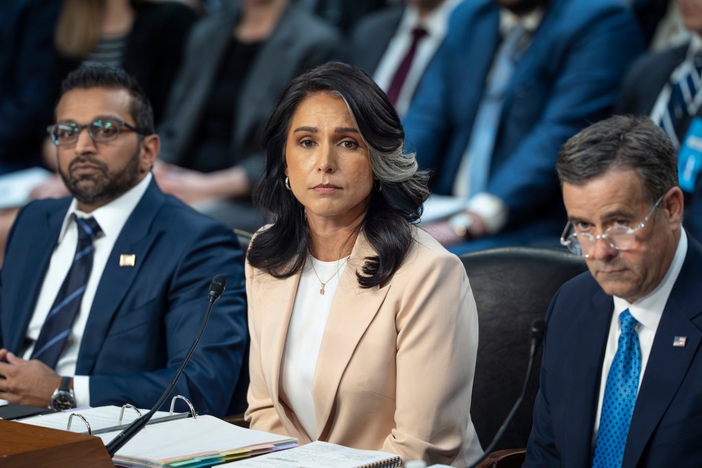 a photo of a woman in a suit sitting at a table with two men in suits surrounding her