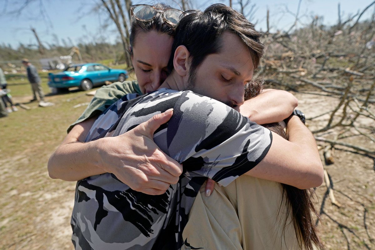 Three people embrace in the middle of a tornado damaged neighborhood