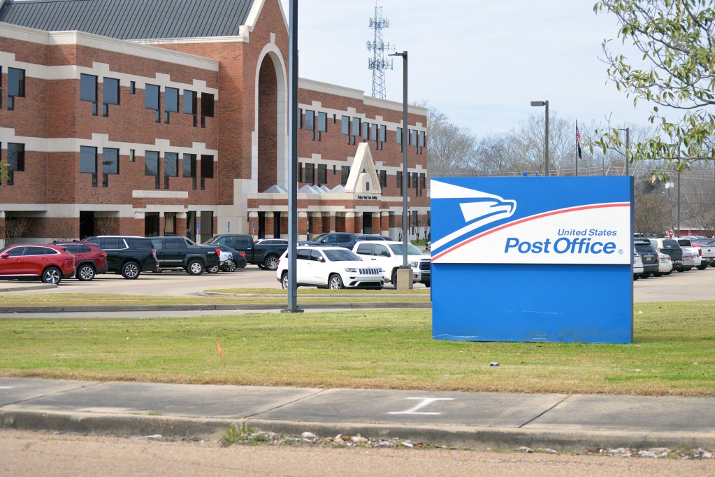 A blue and white sign outside of a large brick building that reads United States Post Office