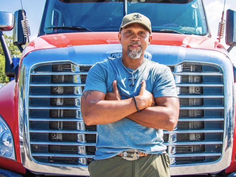 A man stands in front of a red 18 wheeler truck.
