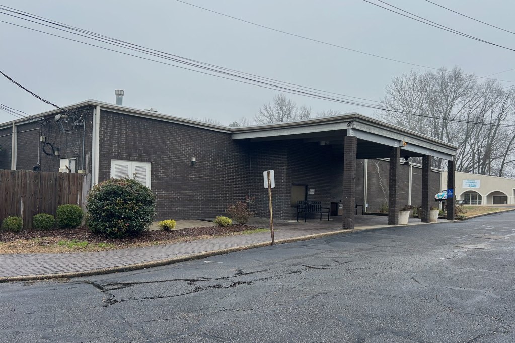 A brown brick building has a black road in front of it.