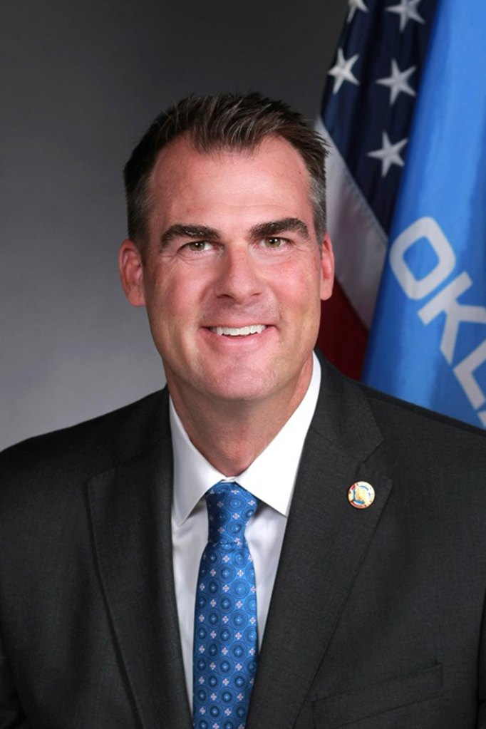 Official portrait of a man in a suit in front of a US and Oklahoma flags
