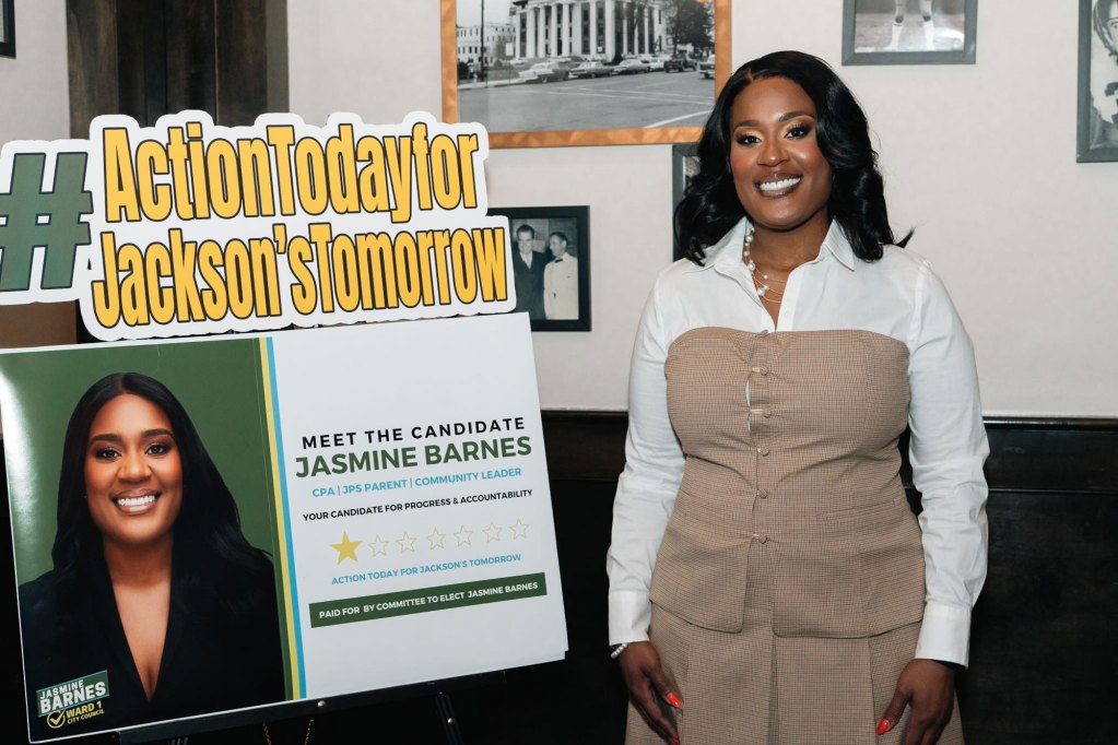 Jasmine Barnes a candidate for Ward 1 stands next to a yellow and green political sign of her own.